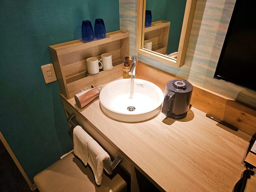 멀티 충전 포트와 화장대가 완비된 객실 내 데스크, 위생적으로 분리된 호텔 윙 구마모토 객실 세면대와 비품